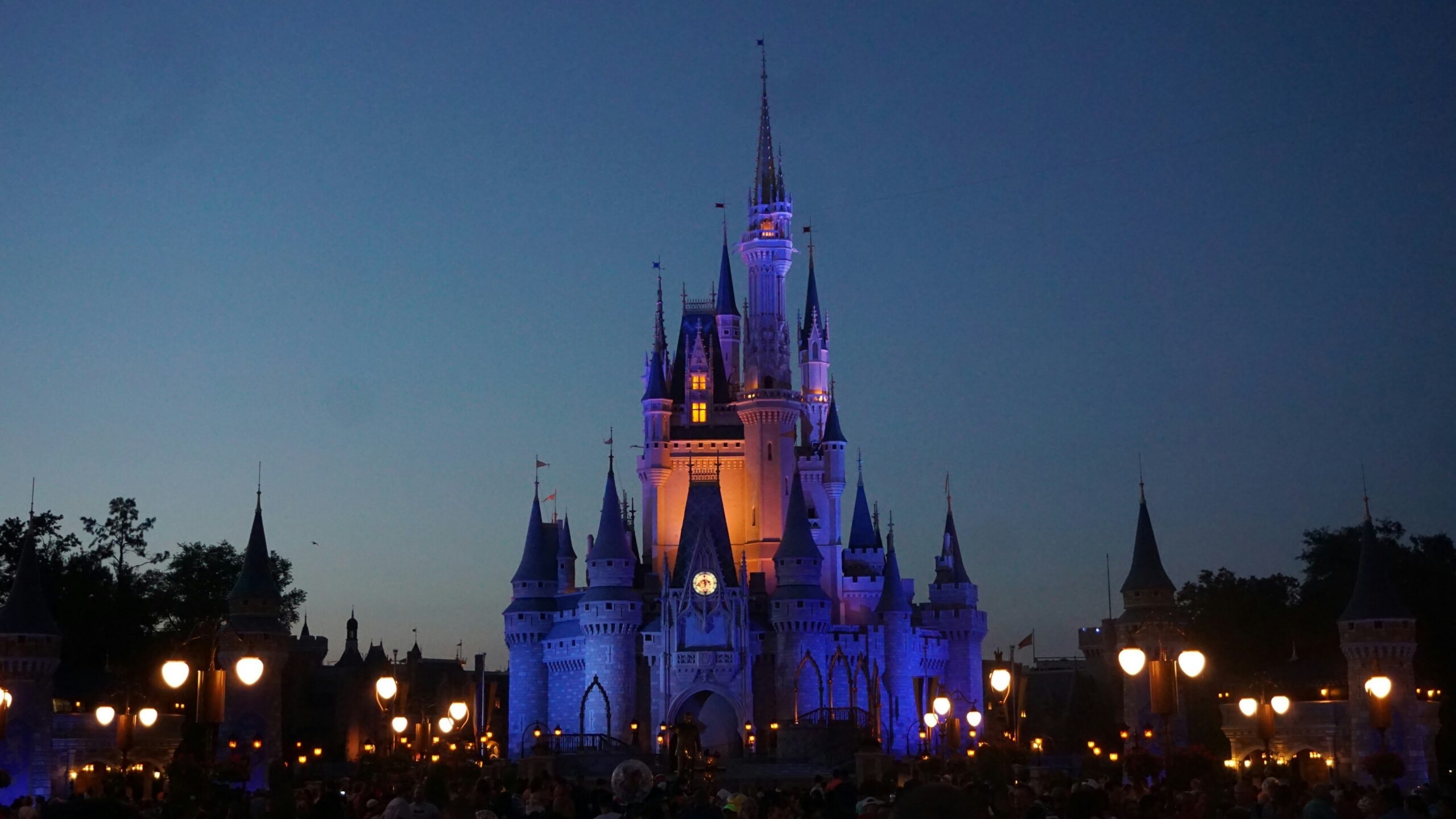 A photograph at dusk of Disney Castle lit up in blue and orange.